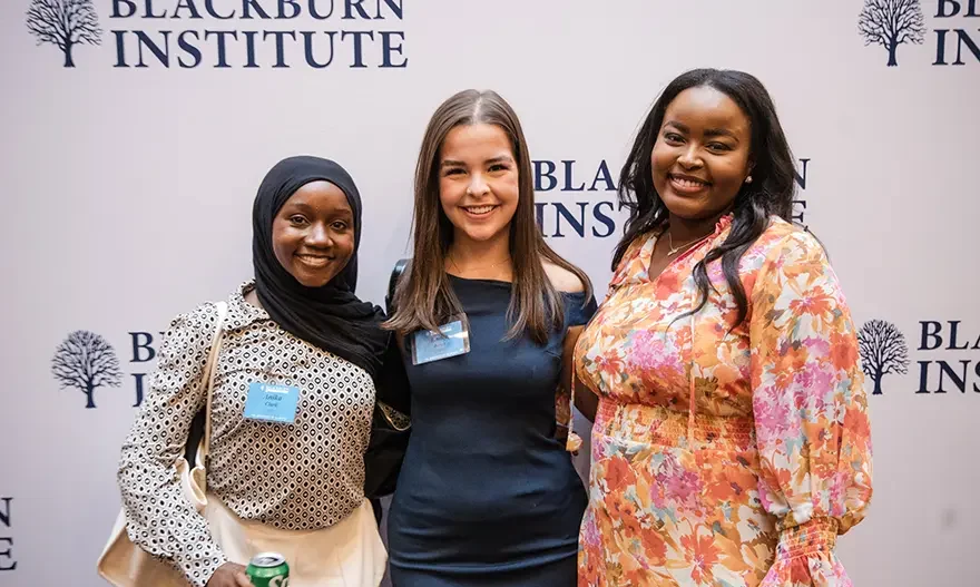 Three women pose in front of a banner with the Blackburn Institute logo printed on it.